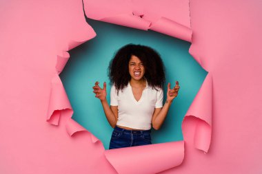 Kırık kağıda sarılmış genç Afrikalı Amerikalı kadın mavi arka planda öfkeyle bağırıyor..