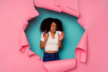 Kırık kağıda sarılı genç Afrikalı bir kadın mavi arka planda izole edilmiş, tiksinti gösteren birini reddediyor..