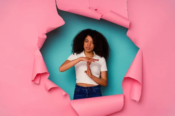 Young African American woman in torn paper isolated on blue background showing a timeout gesture.