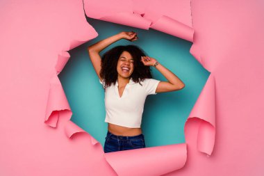 Genç Afrikalı Amerikalı yırtık bir kadın mavi arka planda izole edilmiş özel bir günü kutluyor, atlıyor ve enerji ile kollarını kaldırıyor..