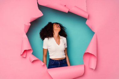 Genç Afro-Amerikan kadın yırtık bir kağıtta mavi arka planda izole edilmiş rahat ve mutlu bir şekilde gülüyor, boynunda dişlerini gösteriyor..