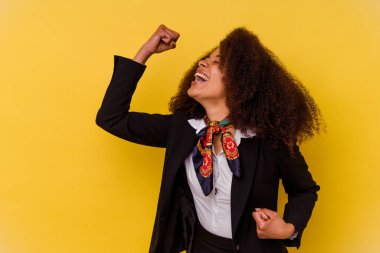 Genç Afrikalı Amerikalı hostes sarı arka planda izole edilmiş zafer ve galibiyet kavramından sonra yumruğunu kaldırıyor..