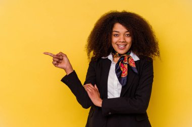 Genç Afrikalı Amerikalı hostes sarı arka planda izole edilmiş. Gülümseyerek işaret parmağıyla işaret ediyor..