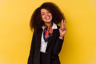 Genç Afrikalı Amerikalı hostes sarı arka planda izole edilmiş zafer işareti gösteriyor ve gülümsüyor..