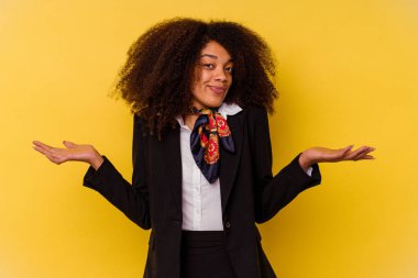 Genç Afrikalı Amerikalı hostes sarı arka planda izole edilmiş sorgulama sırasında omuz silkiyor ve kuşkulanıyor..