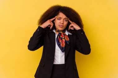 Genç Afrikalı Amerikalı hostes sarı arka planda izole edilmiş olarak bir göreve odaklanmış ve işaret parmaklarını işaret ediyor..