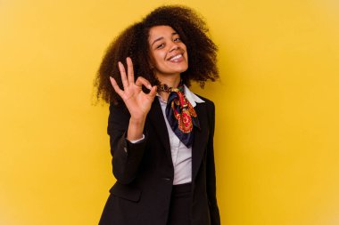 Genç Afrikalı Amerikalı hostes sarı arka planda izole edilmiş neşeli ve kendinden emin bir şekilde iyi bir jest yapıyor..