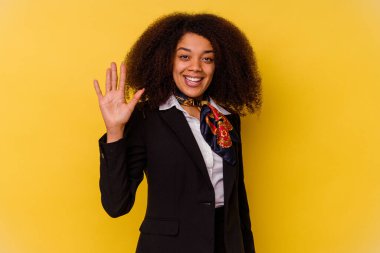 Genç Afrikalı Amerikalı hostes sarı arka planda izole edildi. Gülümseyerek beş numarayı parmaklarıyla gösterdi..