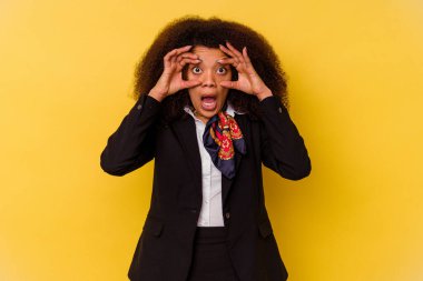 Genç Afrikalı Amerikalı hostes sarı arka planda izole edilmiş bir şekilde gözlerini açık tutarak bir başarı fırsatı arıyor..