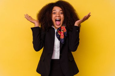 Genç Afrikalı Amerikalı hostes sarı arka planda izole edilmiş bir şekilde zaferi veya başarıyı kutlarken şaşırmış ve şok olmuştu..