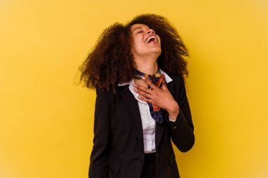 Sarı arka planda izole edilmiş genç Afrikalı Amerikalı hostes elini göğsünde tutarak kahkaha atıyor..