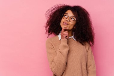 Genç Afrikalı Amerikalı kadın pembe arka planda izole edilmiş şüpheli ve şüpheci bir ifadeyle yana bakıyor..