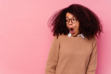 Genç Afrikalı Amerikalı kadın pembe arka planda izole edilmiş. Gördüğü bir şey yüzünden şoka uğruyor..