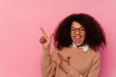 Pembe arka planda izole edilmiş genç bir Afrikalı Amerikalı kadın işaret parmaklarıyla fotokopi alanını işaret ederek heyecan ve arzusunu ifade ediyor..
