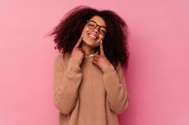 Genç Afrikalı Amerikalı kadın pembe arka planda izole edilmiş gülücükler içinde, parmaklarını ağıza doğrultuyor..