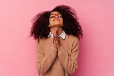 Pembe arka planda izole edilmiş genç Afro-Amerikalı bir kadın el ele tutuşup dua ediyor, kendine güveniyor..