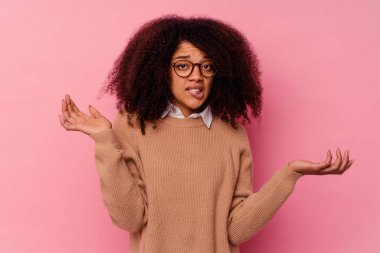 Genç Afrikalı Amerikalı bir kadın pembe arka planda izole edilmiş. Kafası karışmış ve omuz silkiyor. Kopya alanını tutmak için..