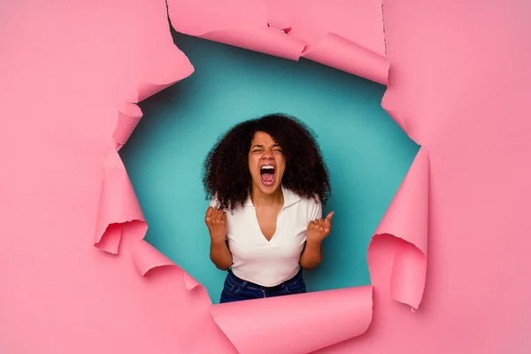 Young African American woman in torn paper isolated on blue background cheering carefree and excited. Victory concept.