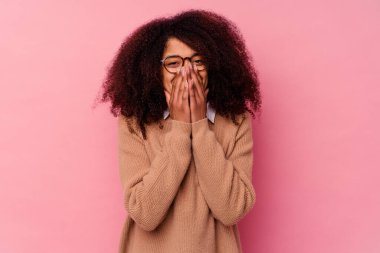 Genç Afrikalı Amerikalı bir kadın pembe arka planda izole edilmiş bir şekilde bir şeylere gülüyor, elleriyle ağzını kapatıyor..