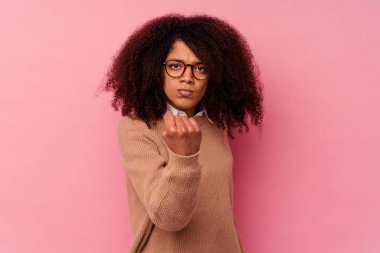 Pembe arka planda izole edilmiş genç Afrikalı Amerikalı kadın yumruğunu kameraya gösteriyor, agresif yüz ifadesi..