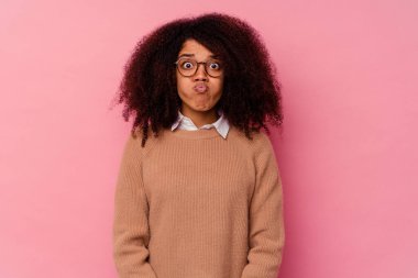 Pembe arka planda izole edilmiş genç Afrikalı Amerikalı kadın yanaklarına üflüyor, yorgun bir ifade takınıyor. Yüz ifadesi kavramı.
