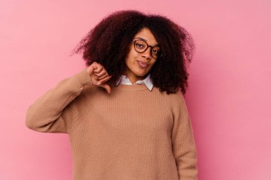 Genç Afro-Amerikalı kadın pembe arka planda izole edilmiş, hoşlanmadığı bir jest gösteriyor, başparmakları aşağıda. Anlaşmazlık konsepti.