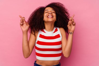 Genç Afrikalı Amerikalı kadın pembe arka planda izole edilmiş şans diliyor.