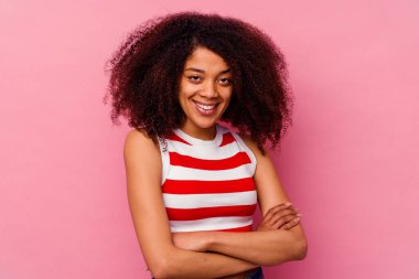 Pembe arka planda izole edilmiş genç bir Afro-Amerikan kadını kendini güvende hissediyor ve kararlılıkla kollarını kavuşturuyor..