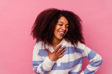 Genç Afro-Amerikalı kadın pembe arka planda izole edilmiş. Gülüyor, elini kalbe koyuyor, mutluluk kavramını koruyor..