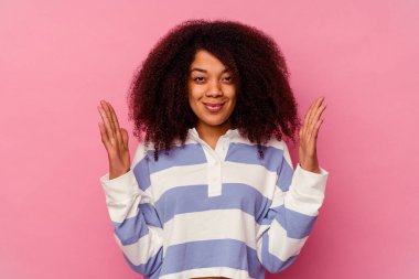 Genç Afrikalı Amerikalı bir kadın pembe arka planda izole edilmiş. Elinde parmakları olan, gülümseyen ve kendinden emin bir şey var..