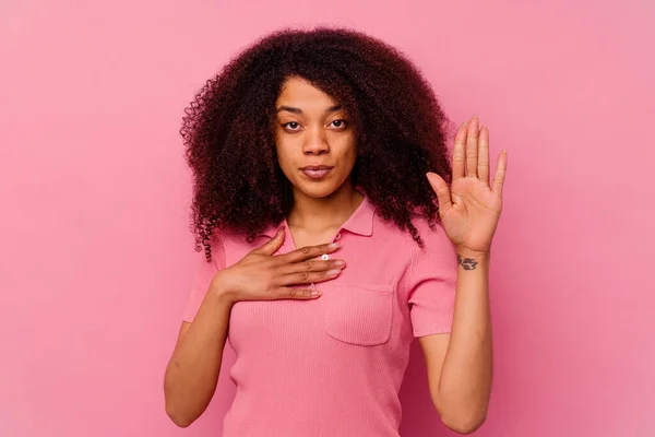 年轻的非洲裔美国女人 背景是粉色的 发过誓 双手放在胸前 — 图库照片
