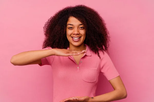 年轻的非洲裔美国妇女 被隔离在粉红的背景下 双手拿着东西 展示产品 — 图库照片
