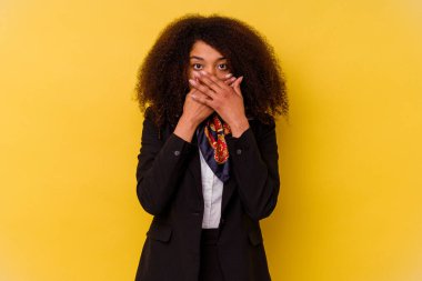 Sarı arka planda izole edilmiş genç Afrikalı Amerikalı hostes elleriyle ağzını kapatırken şok oldu..
