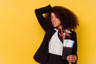 Genç Afrikalı Amerikalı hostes sarı arka planda izole edilmiş uçak biletlerini tutuyor. Başının arkasına dokunuyor, düşünüyor ve bir seçim yapıyor..