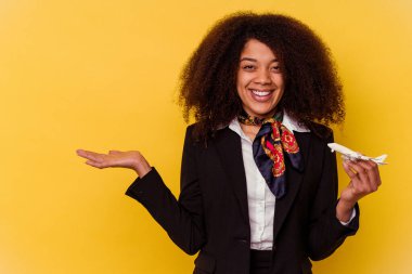 Genç Afro-Amerikan hostes sarı arka planda küçük bir uçak tutuyor. Bir avuç içinde fotokopi alanı var ve belinde başka bir el tutuyor..