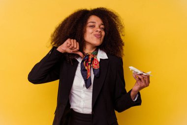 Genç Afrikalı Amerikalı hostes sarı arka planda izole edilmiş küçük bir uçak tutuyor gururlu ve kendinden emin hissediyor, örnek olarak.