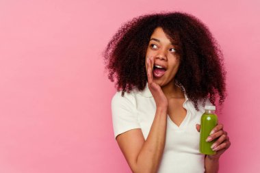 Genç Afrikalı Amerikalı kadın pembe arka planda izole edilmiş sağlıklı bir smoothie içerken gizli bir sıcak fren haberi veriyor ve yan tarafa bakıyor.