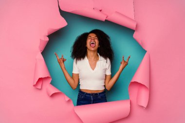 Kırık kağıda sarılı genç Afrikalı kadın mavi arka planda izole edilmiş, parmaklarıyla taş hareketi gösteriyor.