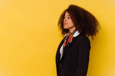 Genç Afrikalı Amerikalı hostes sarı arka planda izole edilmiş, sola bakıyor, yandan poz veriyor..