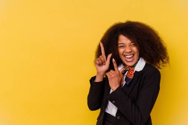 Genç Afrikalı Amerikalı hostes sarı arka planda izole edilmiş ve işaret parmağıyla fotokopi alanını işaret ederek heyecan ve arzusunu ifade ediyor..