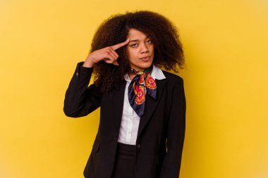 Genç Afrikalı Amerikalı hostes sarı arka planda izole edilmiş. Şakağı işaret ediyor, düşünüyor ve bir göreve odaklanıyor..