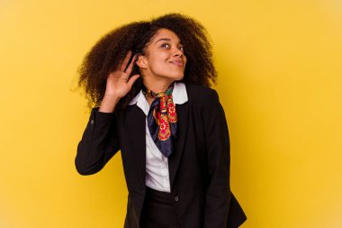 Genç Afrikalı Amerikalı hostes sarı arka planda izole edilmiş bir şekilde bir dedikoduyu dinlemeye çalışıyor..