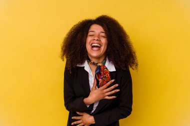 Sarı arka planda izole edilmiş genç Afrikalı Amerikalı hostes mutlu bir şekilde gülüyor ve ellerini karnının üstünde tutarak eğleniyor..