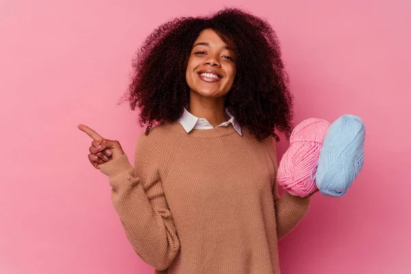 若いアフリカ系アメリカ人の女性は ピンクの背景の笑顔に孤立した縫製糸を持ち 脇を指差して 空白のスペースで何かを示す — ストック写真