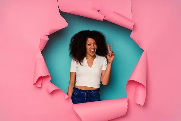 勝利のサインと笑顔を示す青の背景に隔離された破れた紙の中の若いアフリカ系アメリカ人女性 — ストック写真