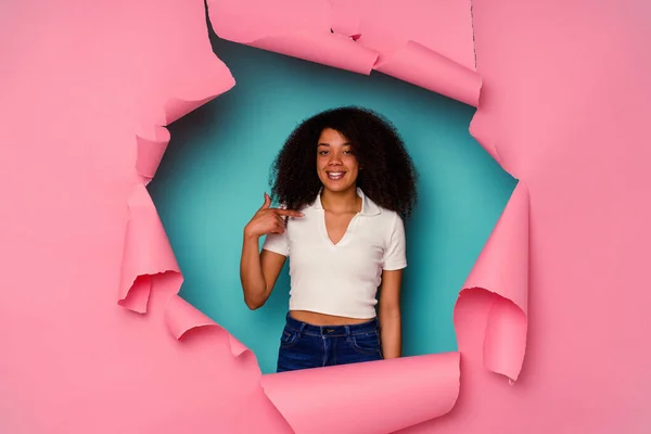 若いアフリカ系アメリカ人女性に引き裂かれた紙の上に隔離された青い背景の人がシャツのコピースペースを指差して 誇りと自信を持って — ストック写真