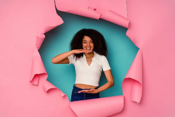 両手で何かを保持青い背景に隔離された引裂かれた紙で若いアフリカ系アメリカ人女性 製品プレゼンテーション — ストック写真
