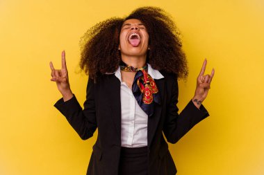 Sarı arka planda izole edilmiş genç Afrikalı Amerikalı hostes parmaklarıyla kaya hareketi gösteriyor.