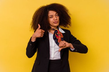 Genç Afrikalı Amerikalı hostes sarı arka planda izole edildi. Baş parmaklarını kaldırdı ve baş parmağıyla işaret etti. Zor seçim konsepti.