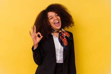 Genç Afrikalı Amerikalı hostes sarı arka planda izole edilmiş bir şekilde göz açıp kapayıncaya kadar iyi bir jest yapıyor..